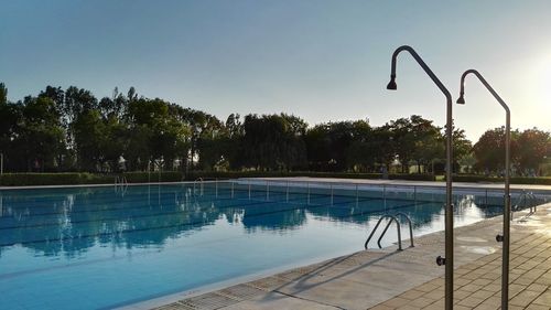 Swimming pool and showers by trees against clear sky