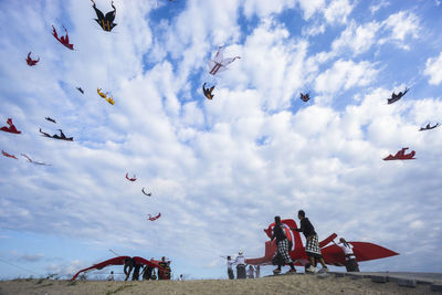 Low angle view of people flying kites against cloudy sky