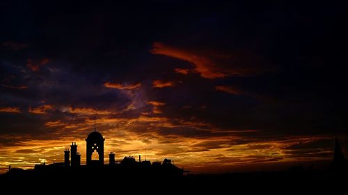 Silhouette structures against dramatic cloudy sky during sunset