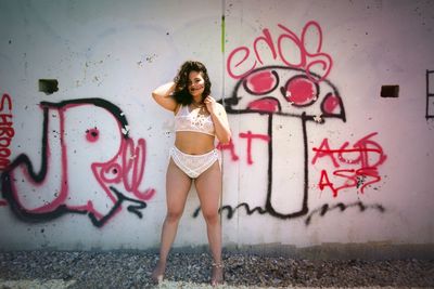 Full length of seductive woman standing against graffiti wall