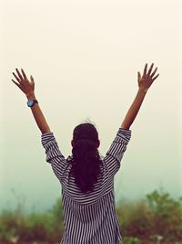 Rear view of woman with arms raised against sky