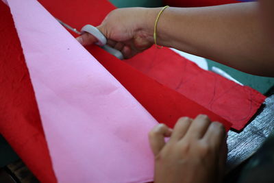 Cropped hands of person cutting red paper on table
