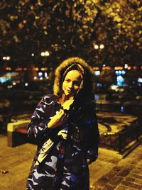 Portrait of woman standing against tree at night