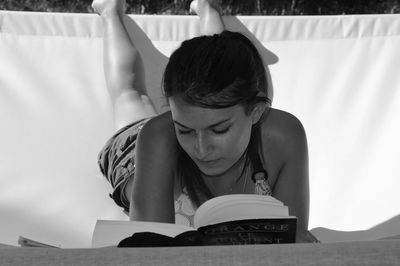 Young woman reading book while lying on hammock