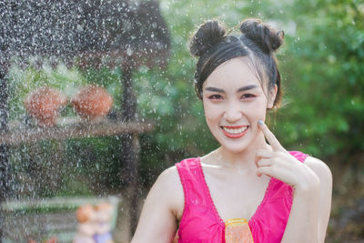 Portrait of smiling young woman by sprinkler against blurred background
