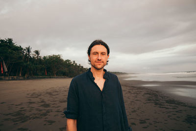 Portrait of young man standing at beach against sky