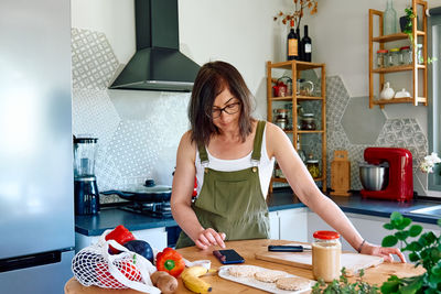 Woman enjoying her healthy breakfast checking on her smart phone at home.