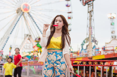 Portrait of young woman eating flavored ice while standing in amusement park