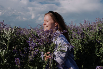 Side view of woman with purple flowers against sky