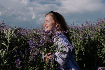 Caucasian smiling young woman holding purple flowers bouquet in field