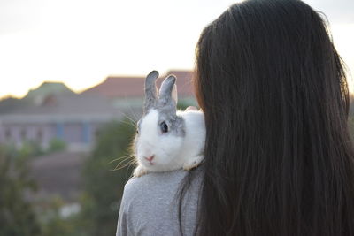 Rear view of woman with rabbit on shoulder against sky