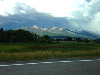 Country road by mountains against cloudy sky