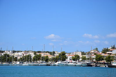 Sailboats in sea by buildings against blue sky