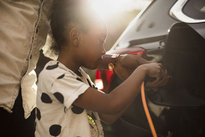 Midsection of man assisting daughter in charging electric car on driveway