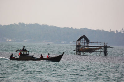 Fishermen sailing boat in sea against sky