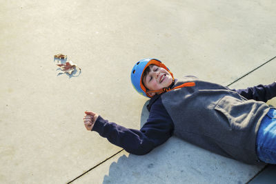 Above view of young skater wearing blue helmet lying on ground smiling