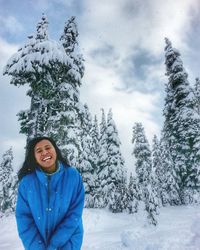 Portrait of cheerful young woman standing against trees in winter