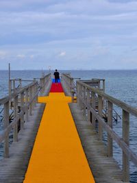 Rear view of woman standing on pier at beach against sky