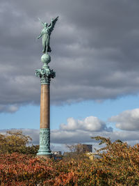 Low angle view of a bronze statue on an ornate column against sky.