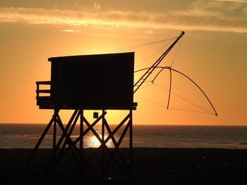 Silhouette hut on beach against sky during sunset