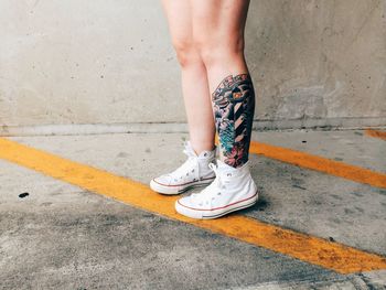 Low section of woman with tattoo standing on footpath