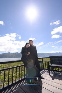 Man standing on railing against sky on sunny day