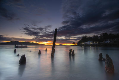 Silhouette people on wooden post in sea against sky during sunset