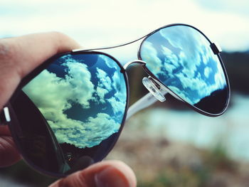 Close-up of hand holding sunglasses against sky