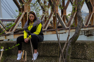 Full length of young woman standing against trees on bridge