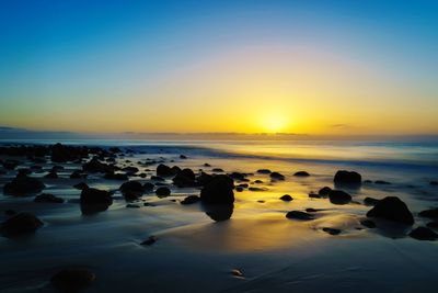 Rocks on beach against sky during sunset