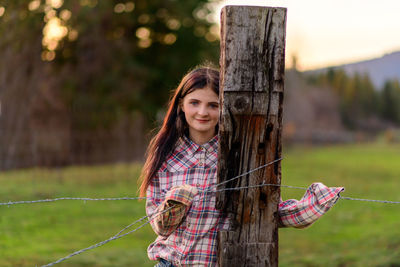 Portrait of young woman standing by barbed wire fence