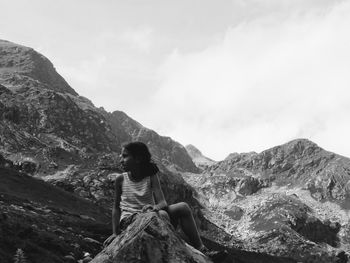 Rear view of woman sitting on rock against mountain