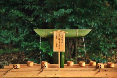 Close-up of japanese text on table and traditional bamboo fountain against trees