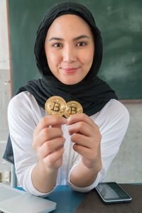 Portrait of smiling woman in hijab holding bitcoin at home
