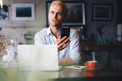 Mid adult man using smart phone while sitting on table