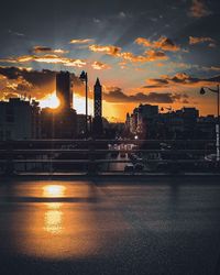 City by river against sky during sunset