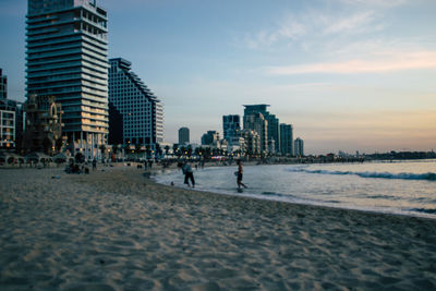 Scenic view of beach by buildings against sky during sunset