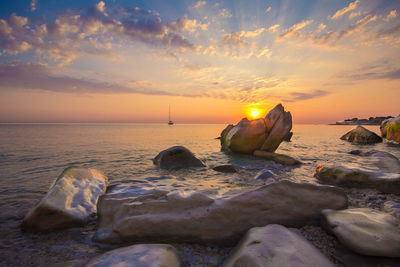 Rocks on beach against sky during sunset