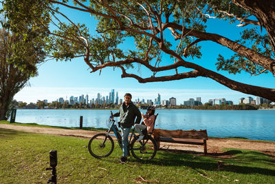 Side view of man sitting on bench by lake against sky