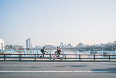 People riding bicycle on road in city against clear sky