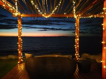 Illuminated chair by sea against sky at night