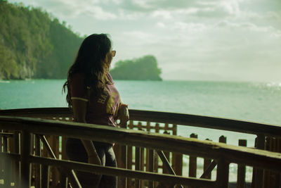 Woman standing by railing against sea