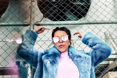 Portrait of woman wearing sunglasses against chainlink fence