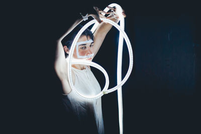 Mid adult woman holding illuminated fiber optic cable in darkroom