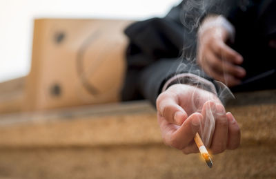 Businessman wearing paper bag and holding cigarette while lying on floor