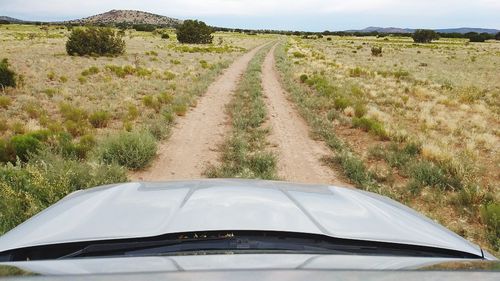 Dirt road amidst field against sky