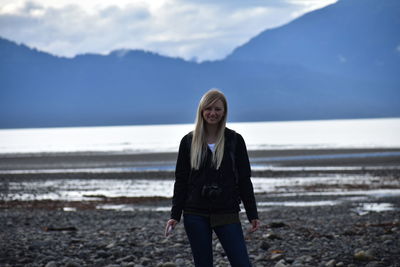 Portrait of teenage girl standing at beach against sky