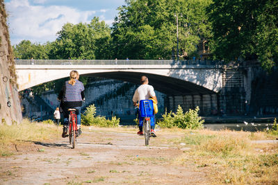 Rear view of man and woman riding bicycles on field