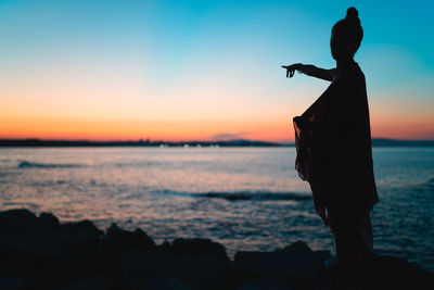 Silhouette person standing on rock at beach during sunset