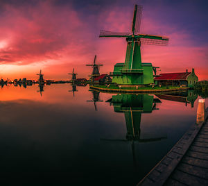 Traditional windmills by lake against sky during sunset